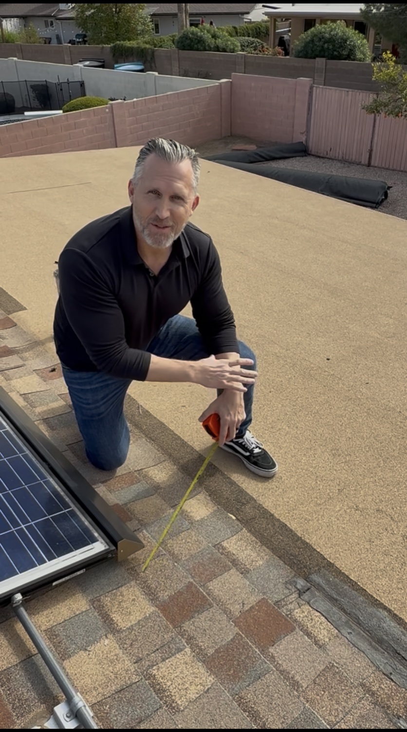 Bryan measuring a low-slope roof beside a solar array — back to real roofs