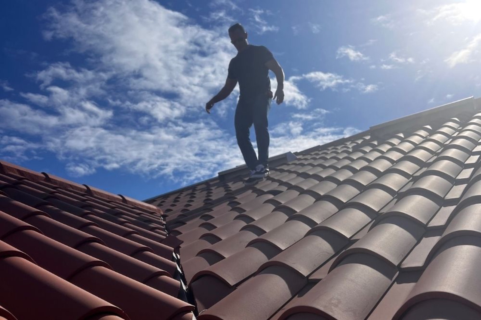 Bryan Stephens walking a tile roof against a bright Arizona sky